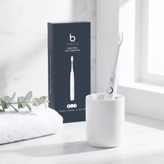 Bianca Electric Toothbrush in a ceramic cup with its box on a marble bathroom counter