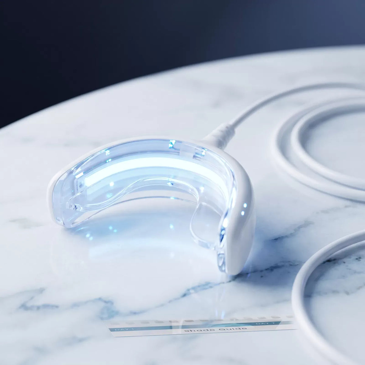 Macro of the Bianca Bright wired LED whitening tray glowing blue on marble
