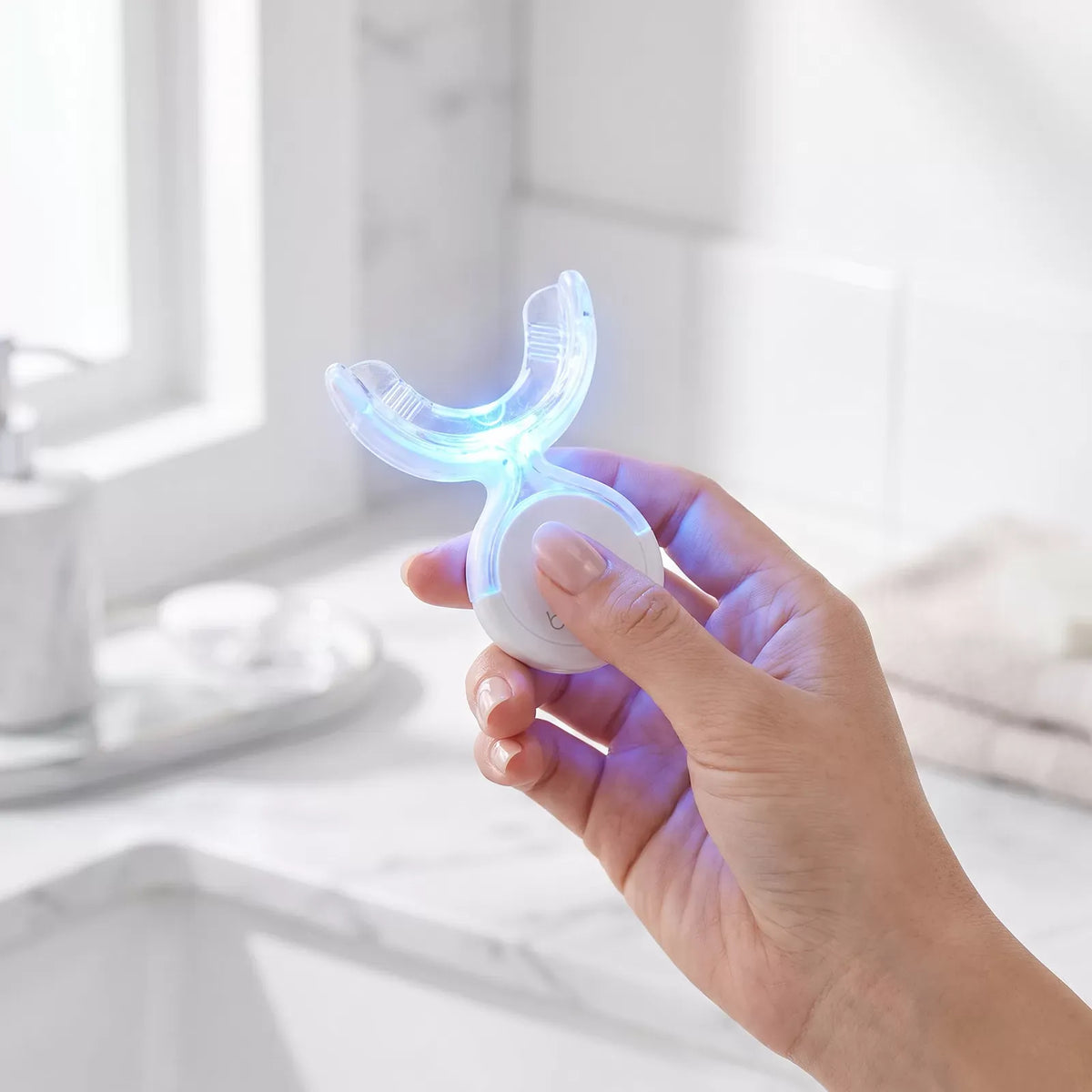 Hand holding the Bianca Bright wireless LED whitening mouthpiece glowing blue