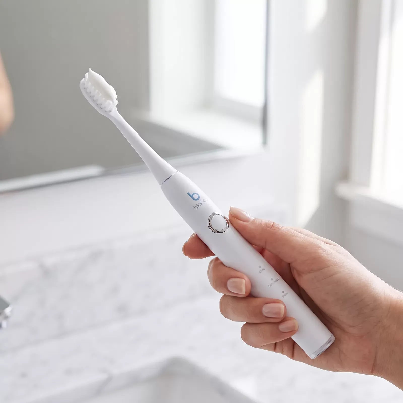 Hand holding the Bianca Electric Toothbrush with toothpaste applied to the bristles