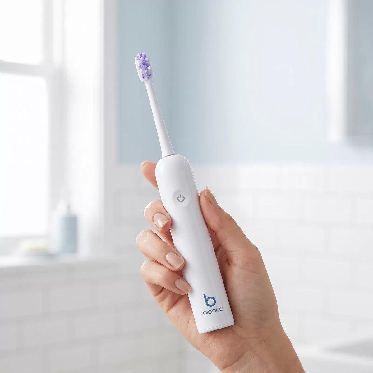 Hand holding the Bianca Oscillating Electric Toothbrush in a bright bathroom