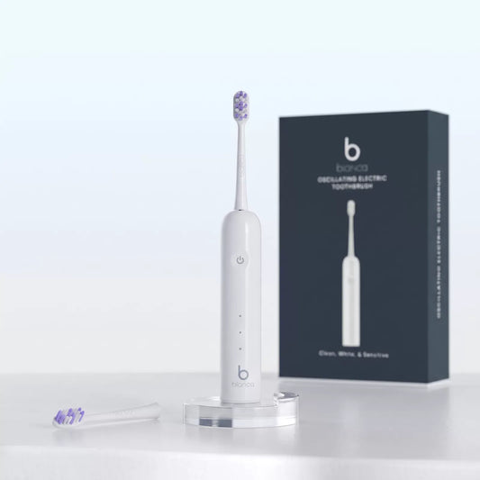 Bianca Oscillating Electric Toothbrush on its charging stand with spare brush head and box