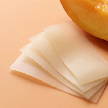 Thin translucent ivory collagen oral strips fanned out next to a mango