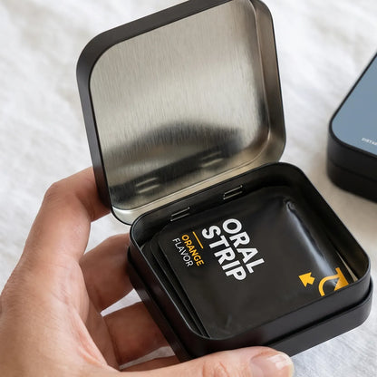 Hand holding an open tin of orange biotin oral strip packets