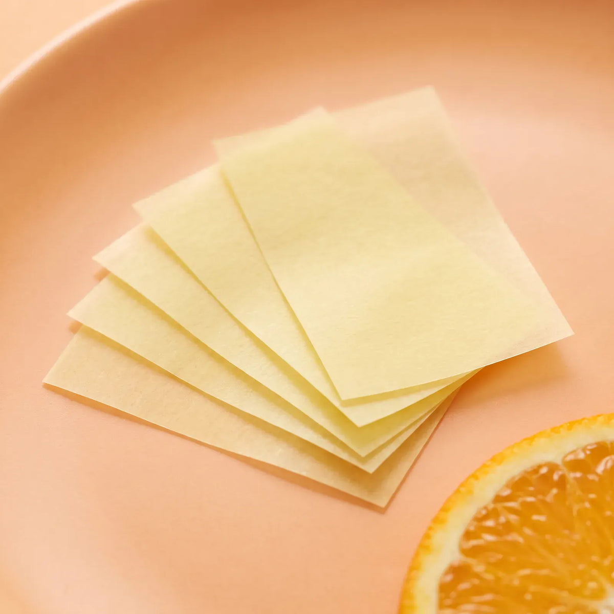 Thin translucent pale yellow biotin oral strips fanned out next to an orange slice
