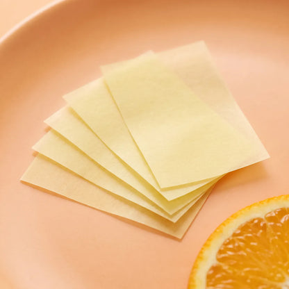 Thin translucent pale yellow biotin oral strips fanned out next to an orange slice